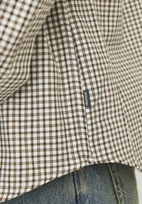 Kockás ing, fehér és barna mintával, puha tapintású anyagból készült. Tartalmaz egy kis címkét "JACK & JONES" logóval.