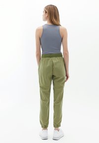 Olivgrüne, elastische Hosen mit umschlägigen Knöcheln, aus einem weichen, leichten Stoff gefertigt. Kombiniert mit einem taillierten grauen Tanktop.