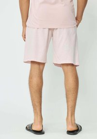 Shorts en lin rose clair avec une coupe décontractée, présentant une texture unie et une coupe droite, associés à des sandales à glissière noires.