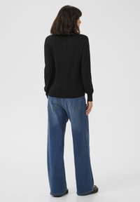 Maglioncino nero a maniche lunghe abbinato a jeans a gamba larga blu chiaro a vita alta. Il tessuto è liscio con una vestibilità comoda e dettagli minimi.