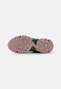 Schwarze Gummisohle mit einer strukturierten, rosa Außensohle, die ein geometrisches Muster und einen roten Akzent aufweist. Verfügt über Haftungsrippen für besseren Grip.