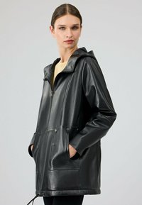 Giacca in pelle nera con cappuccio, chiusura con zip e due tasche frontali. Presenta una texture liscia e cuciture a pannello in contrasto.