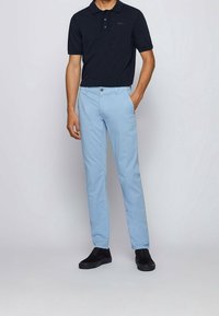 Tmavě modrá polo tričko s krátkými rukávy a třemi knoflíky; spárováno se světle modrými kalhotami a černými semišovými botami. Jednoduchý design, přiléhavý střih.