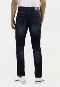 Donkerblauwe denim jeans met een slim fit, voorzien van achterzakken en een leren taillebandlabel. Zichtbare stiksels en een lichte vervaging bij de benen.