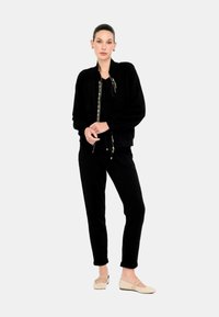 Giacca bomber nera in maglia con chiusura a zip, abbinata a pantaloni neri aderenti. Gli accessori includono scarpe basse beige.