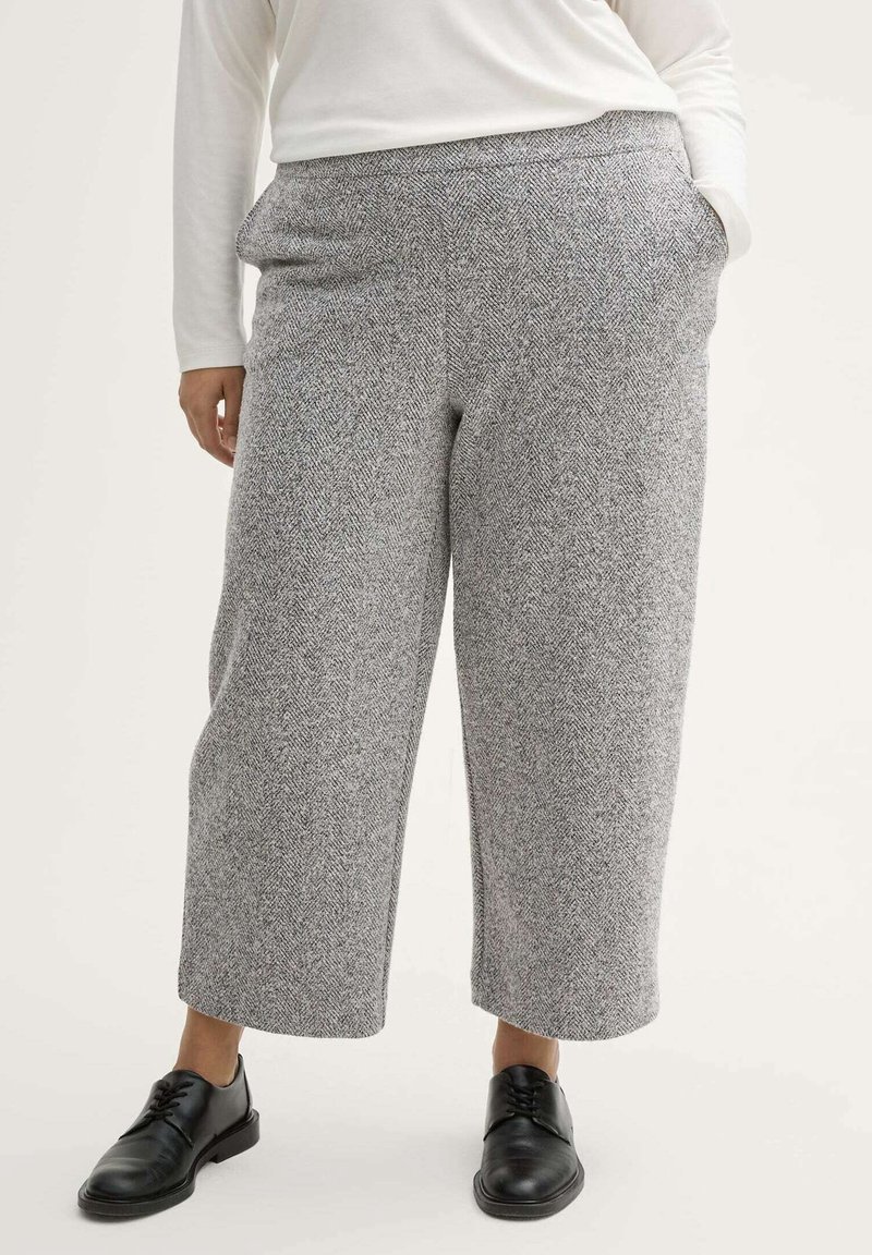 Pantalon large à motif pied-de-poule gris avec poches latérales et taille élastiquée, assorti à des chaussures noires à lacets. Les tissus semblent doux.