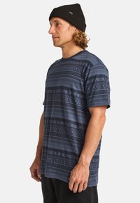 Navy patterned t-shirt with horizontal stripes and geometric designs, made from soft fabric, worn with a black beanie, displaying a relaxed fit.