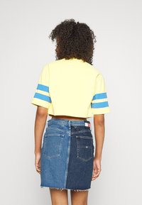 Avskuren gul t-shirt med blå ränder på ärmarna, kombinerad med en denimkjol med ljusa och mörka blå paneler, fransad fåll och bakfickor.