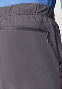 Grå idrottsbyxor med elastiskt midjeband och en sidoficka med dragkedja, tillverkade av ett mjukt, lätt tyg med subtil textur.