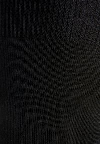 Calzini alti neri a coste con una consistenza fine, dotati di una banda superiore liscia e un design a costine verticali lungo tutto il corpo.
