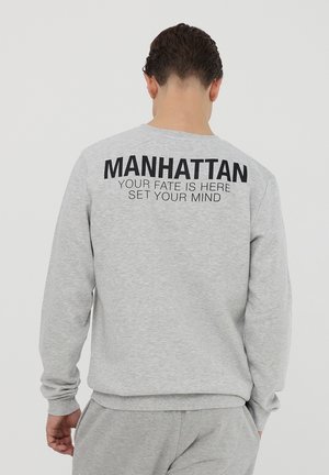 Felpa grigia con testo nero sul retro: "MANHATTAN IL TUO DESTINO È QUI METTI A FUOCO LA TUA MENTE." Tessuto morbido, polsini e orlo a coste.