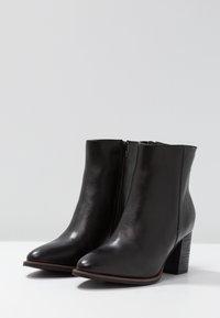 Botas de tobillo de cuero negro con punta afilada y cremallera lateral. Cuentan con un tacón bloque y una textura suave.