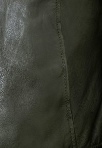 Dunkelgrüne Ledertextur mit glatter, leicht glänzender Oberfläche. Sichtbare Nähte entlang der Naht verleihen dem Design Details.