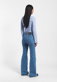Light blue ribbed long-sleeve top paired with medium-wash flared jeans. The jeans feature a back label and a relaxed silhouette.