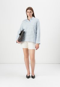 Striped long-sleeve shirt in light blue and white, paired with white shorts and black flats. Holding a dark brown handbag.