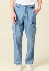 Vaaleansiniset farkkucargo-housut, joissa on sivutaskut, rento malli ja hieman haalistunut pinta. Yhdistetty valkoisiin lenkkitossuihin.