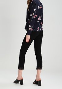 Blusa blu navy con stampa floreale, abbinata a pantaloni neri a cropped con frange all'orlo e mule neri con tacco a blocco.