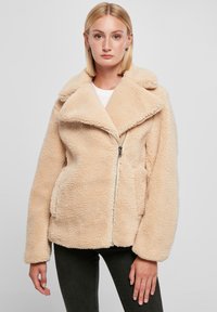 Beige fleece jack met een brede kraag, ritssluiting en twee zijzakken. Zachte textuur en een ontspannen pasvorm met verlaagde schouders.