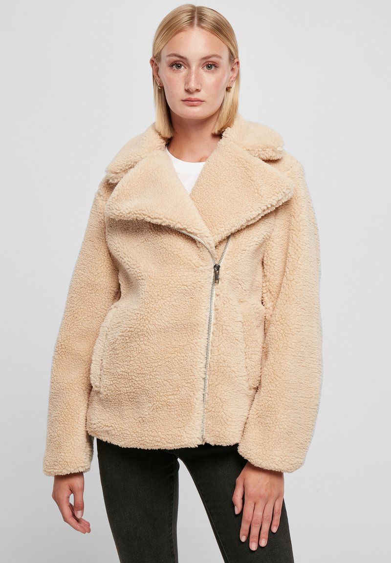 Beige fleece jack met een brede kraag, ritssluiting en twee zijzakken. Zachte textuur en een ontspannen pasvorm met verlaagde schouders.