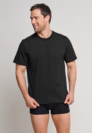 Schwarzes Baumwoll-T-Shirt mit kurzen Ärmeln und rundem Ausschnitt, präsentiert an einem Mann, der schwarze Unterwäsche trägt, mit einem entspannten Schnitt.