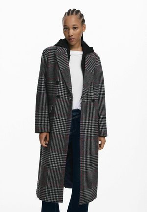 Gray checkered coat with black accents, double-breasted design, long sleeves, and side pockets. Worn over a black hooded sweatshirt.