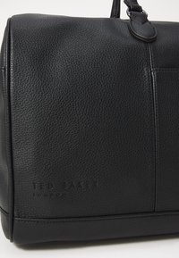 Black leather handbag with a pebbled texture, featuring subtle branding, a structured shape, and a detachable strap.