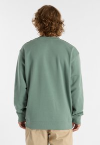 Pullover verde con scollatura a girocollo, maniche lunghe e tessuto testurizzato. Il design presenta polsini a costine e una vestibilità rilassata.