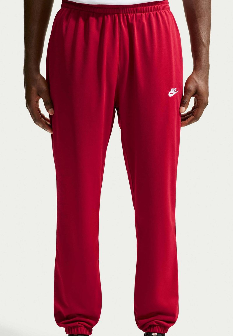 Uomo che indossa pantaloni della tuta rossi Nike con elastico in vita e ai polsi, in piedi con le mani rilassate ai lati.