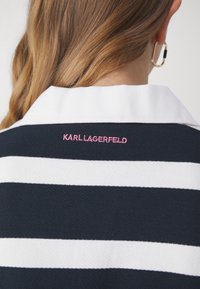 Polo a rayas en azul marino y blanco con cuello blanco y bordado en rosa "KARL LAGERFELD" en la espalda. Tejido suave al tacto.
