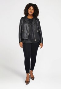 Czarna skórzana kurtka motocyklowa z srebrnymi zamkami w kieszeniach, zestawiona z czarnym topem i legginsami. Całość dopełniają szpilki w panterkę.
