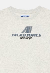 T-shirt grigio chiaro con collo a giro. Presenta il testo "JACK&JONES" e "core dept." stampato in grafica blu scuro. Texture morbida.