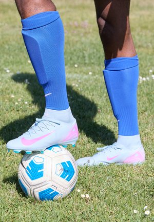 Jasnoniebieskie korki piłkarskie z różowymi akcentami, niebieskie skarpety sportowe i wzorzysta piłka nożna na trawie.
