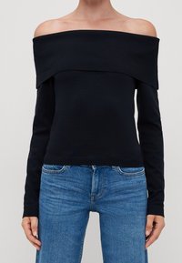 Haut noir à épaules dénudées avec encolure côtelée et manches longues. Présente un corsage ajusté et une texture douce. Associé à un jean denim bleu.