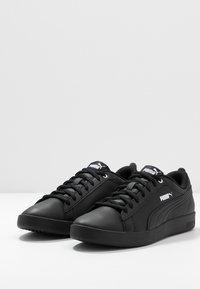 Zapatillas negras con parte superior de cuero sintético, puntera redonda, cordones planos, cuello acolchado y acentos de logo blanco en la lengua y en el lateral.