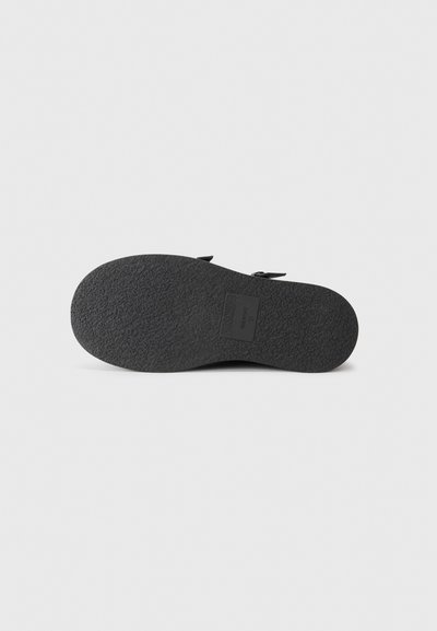 Black textured rubber sole of a sandal with visible brand label and size number 37, shown on a light gray background.