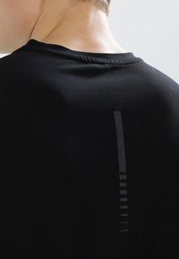 Camiseta deportiva negra con una tela texturizada, un escote redondeado y un acento vertical brillante en la parte posterior con detalles lineales.