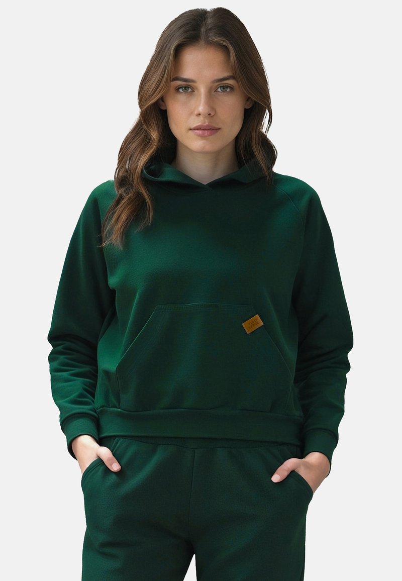Sudadera de un verde oscuro con un bolsillo tipo canguro, puños y dobladillo acanalados, hecha de una tela suave. Cuenta con un pequeño parche de logo en color beige.