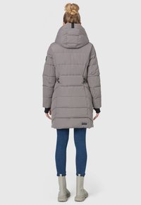 Grå polstret frakke med en stor hætte, justerbare side stropper og lynlås lommer. Sammen med blå jeans og grå ankelstøvler.