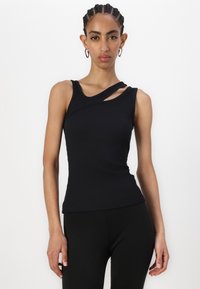 Zwarte geribbelde tanktop met een asymmetrische halslijn en een enkele schouderband, strakke pasvorm en textuurstof. Geloofd met zwarte leggings.