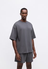 Sweatshirt gri cu mânecă scurtă, lejer, și pantaloni scurți asortați, dintr-un material moale; prezintă un guler rotund și un branding subtil pe piept.