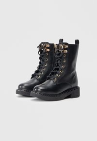 Botine negre din piele, cu detalii aurii, design cu șireturi și finisaj texturat. Prezintă un toc masiv și accente decorative.