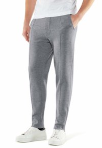 Grijze sweatpants met een taps toelopend ontwerp, zijzakken en gestikte details, gedragen met witte sneakers. Zachte stofstructuur.