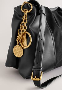 Mustast nahast käekott pehme tekstuuriga, millel on kuldne kett, ümmargused detailid ja kuldsed aksendid. Reguleeritav rihm ja struktureeritud kuju.