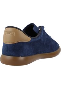 Marineblaues Wildleder-Sneaker mit akzentuierter Ferse aus hellbraunem Leder, runder Zehenpartie, weicher Textur und flexibler Gummisohle. Markenname auf der Ferse geprägt.