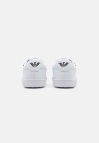 Hvite lær sneakers med lavt design, teksturert såle, rund tå og svarte logo detaljer på hælen.