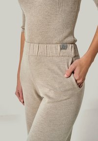 Beige gerippte Strickhose mit elastischem Bund, Seitentaschen und Logopatch. Weicher Stoff mit taillierter Passform, geeignet für legere Outfits.