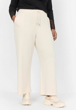 Light beige wide-leg sweatpants with a drawstring waistband, side pockets, and a smooth texture, paired with light sneakers.