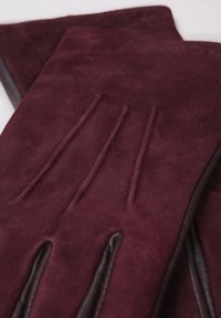 Burgundy suede gloves feature three stitched lines on the back, with contrasting brown leather accents along the cuffs. Smooth texture.