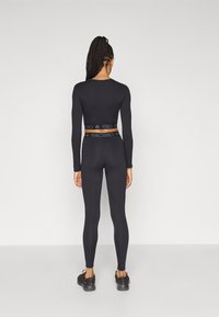 Haut noir à manches longues et leggings ajustés, fabriqués en tissu extensible, avec une ceinture de marque et une texture lisse. Des chaussures de sport complètent le look.