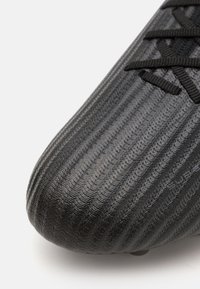 Botín de fútbol negro con una superficie texturizada que presenta estrías horizontales, material ligero y cordones negros. Diseñado para el rendimiento.